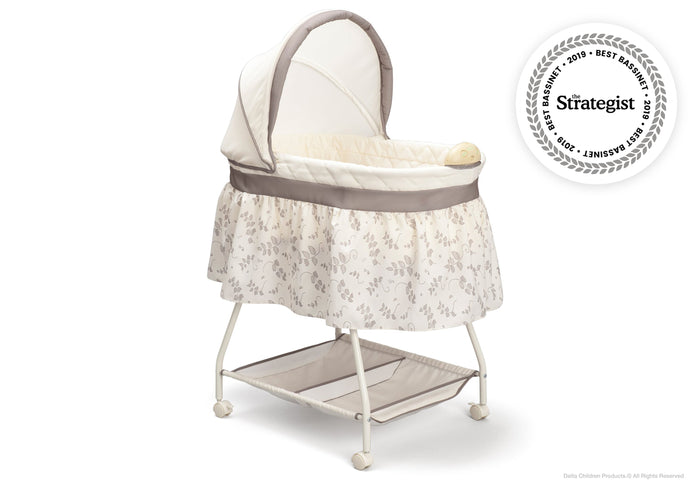 A white and beige Deluxe Sweet Beginnings Bassinet with a fitted sheet, removable canopy, storage basket underneath, and locking wheels.