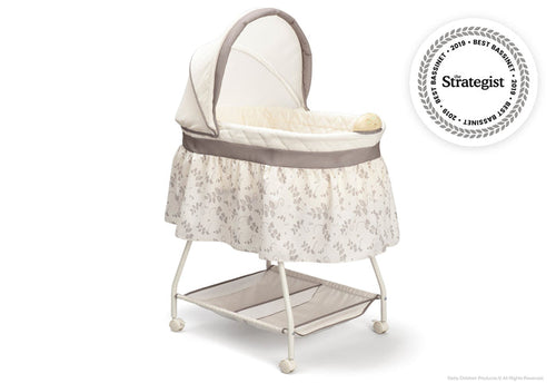 A white and beige Deluxe Sweet Beginnings Bassinet with a fitted sheet, removable canopy, storage basket underneath, and locking wheels.