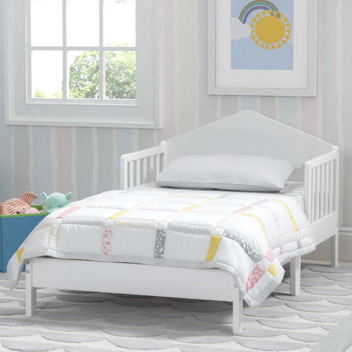 White children's bed with colorful bedding in a room with a window and wall art.